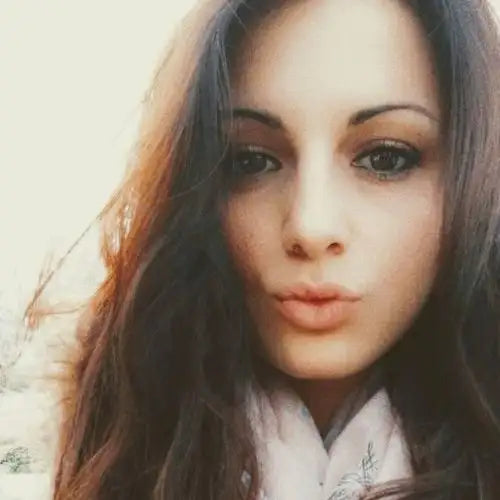 Une femme aux cheveux longs, châtains foncés et au maquillage subtil, portant un haut de couleur claire.